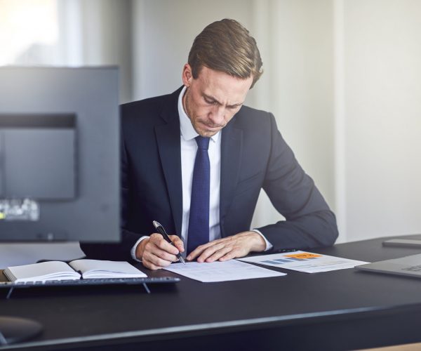 Businessman reading through paperwork at his office desk Businessman sitting alone at his desk and going over notes and paperwork while working in a bright modern office